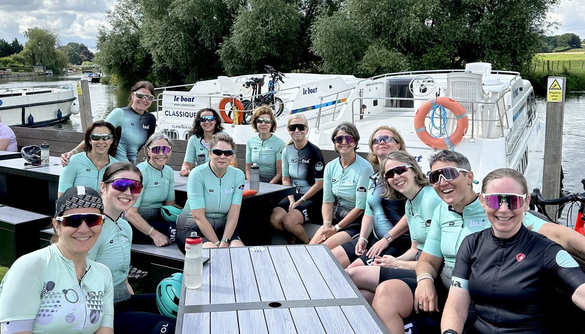 Bia Cycling riders in club kit, all smiles at a riverside stop